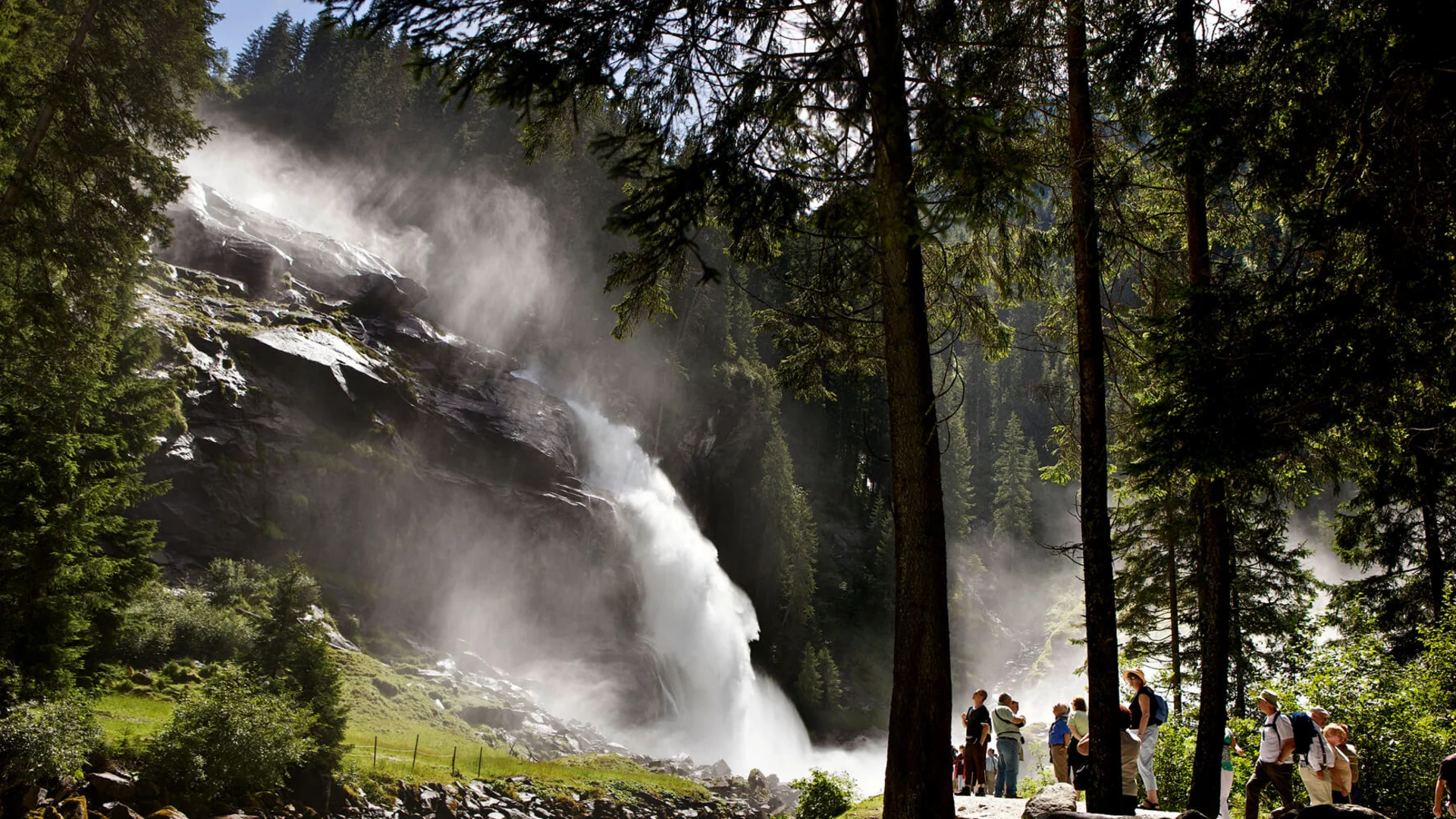 Touristen beobachten einen großen Wasserfall im Wald bei Sonnenschein
