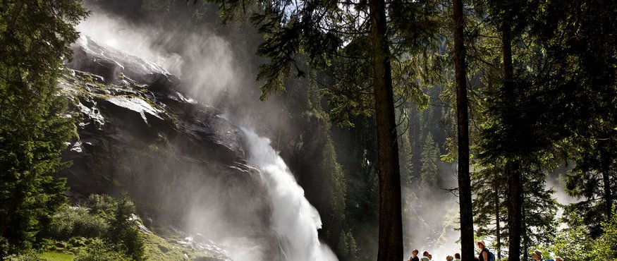 Tourists watching a large waterfall in a sunny forest setting