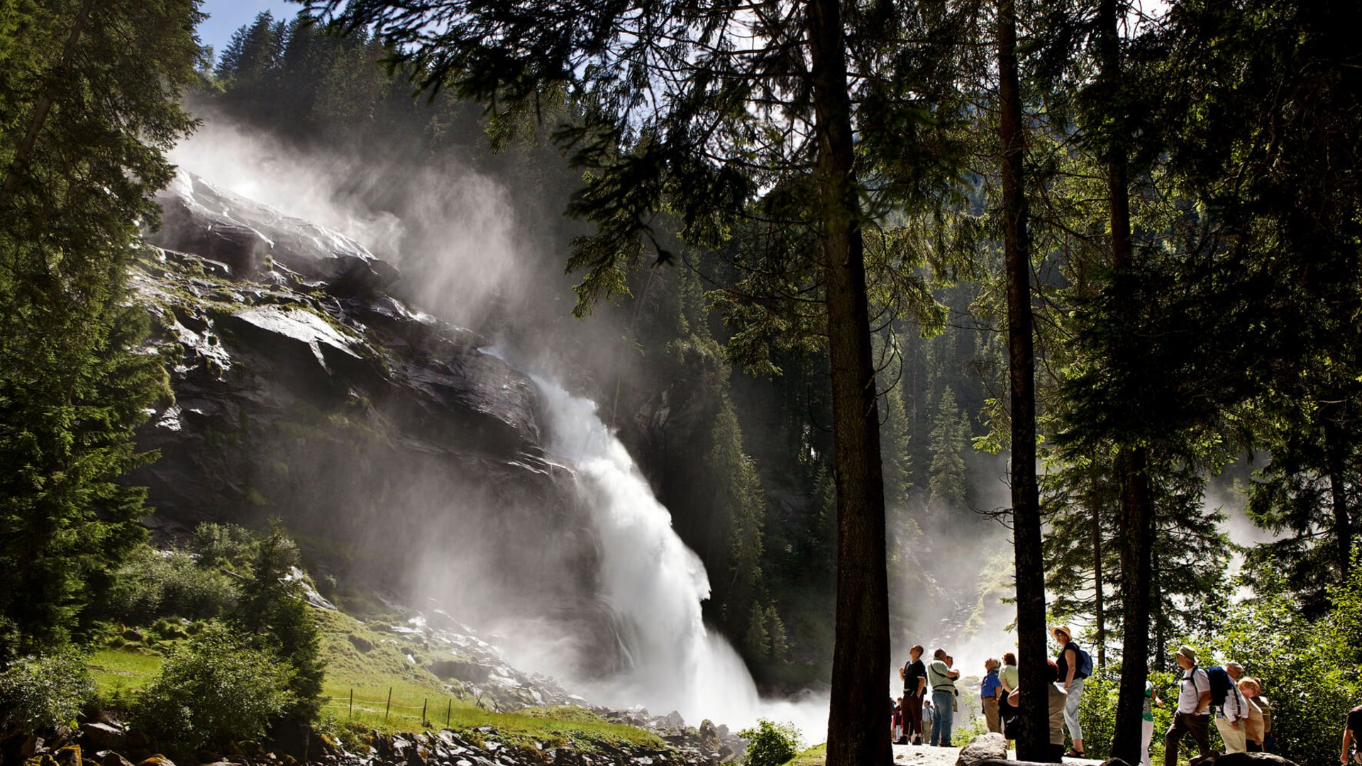 Tourists watching a large waterfall in a sunny forest setting