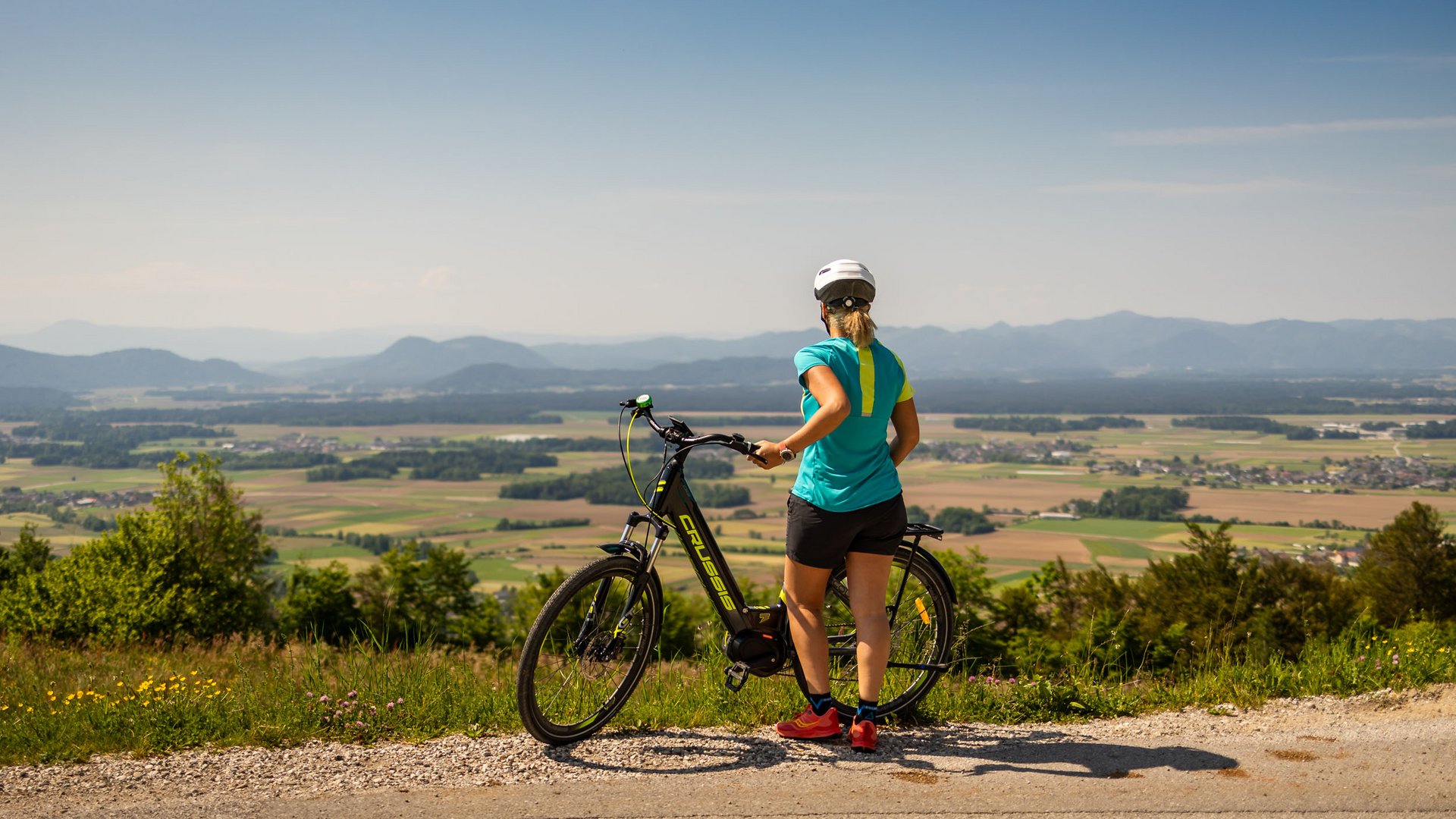 Woman with bicycle overlooking valley and mountains under clear sky