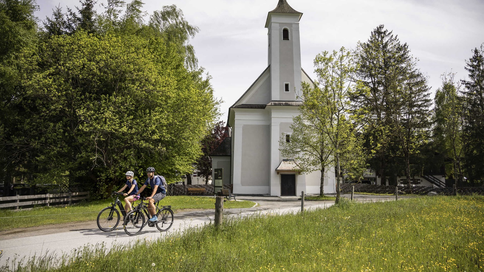 Two cyclists riding on path beside a small white church