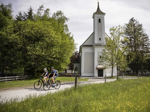 RadGENUSS im kleinen Juwel Maishofen © Velontour Zwei Radfahrer fahren auf einem Weg neben einer kleinen Kirche