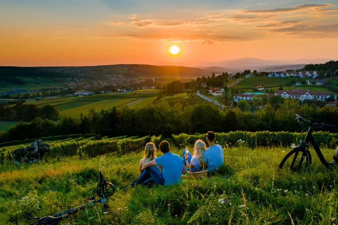Vier Personen sitzen auf einer Wiese und schauen auf den Sonnenuntergang über dem Dorf