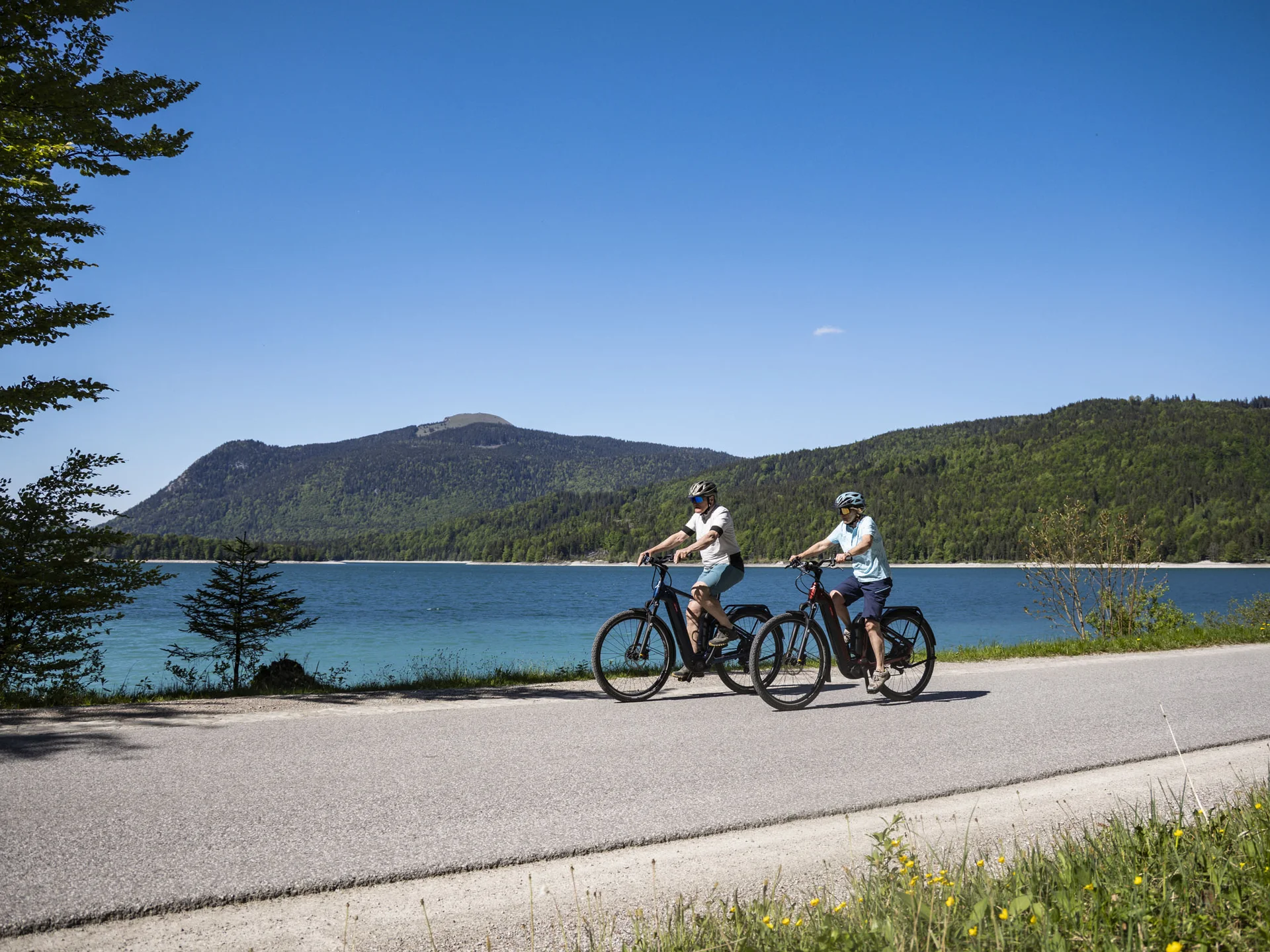 Twee fietsers rijden langs een meer met bergen op de achtergrond