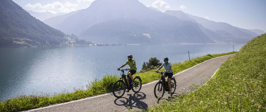 Drei Länder, du und dein Rad: Den Reschensee grenzüberschreitend entdecken © Heiko Mandl Zwei Radfahrer auf Seeweg mit Bergen im Hintergrund