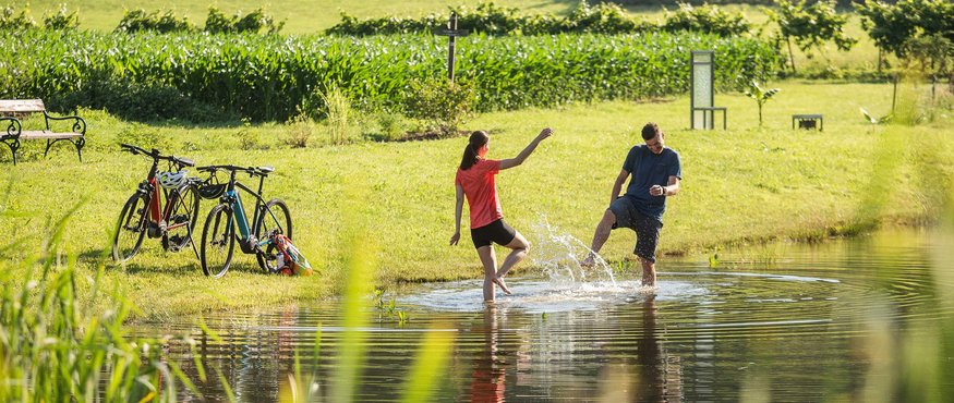 Two people splashing water in a pond near bikes on a grassy field