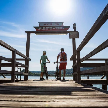Twee fietsers op een steiger bij een meer onder zonnig licht