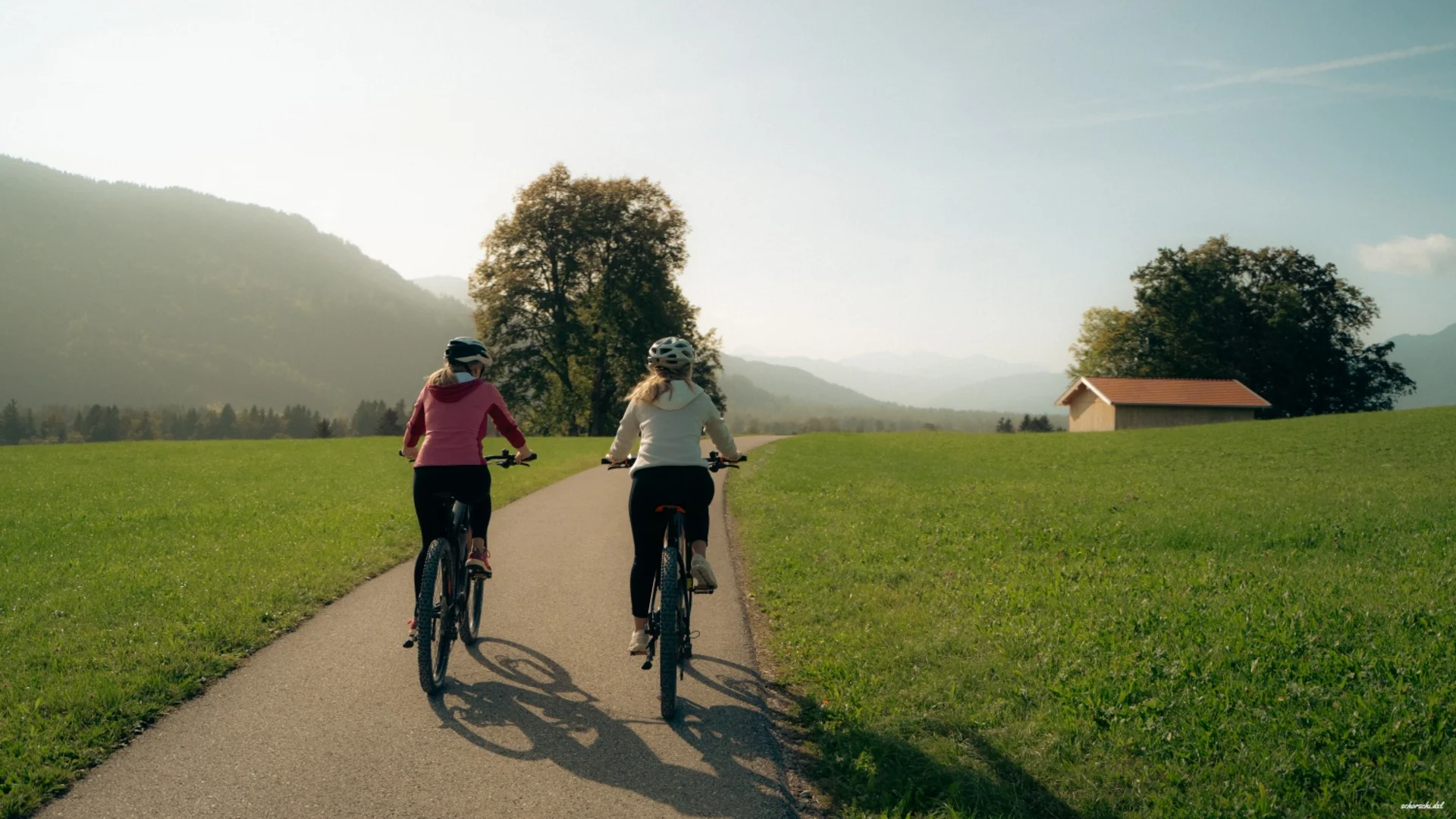 Zwei Frauen fahren auf Radweg durch grüne Landschaft mit Bergen im Hintergrund