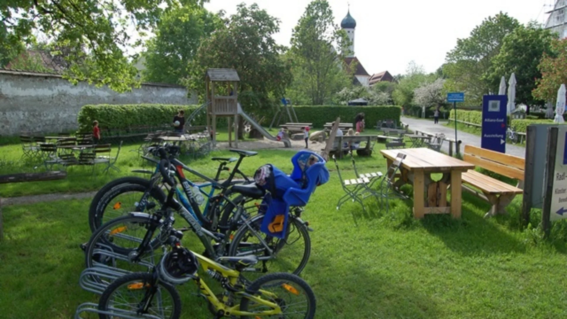 Fahrräder und Kindersitz neben Spielplatz und Sitzgelegenheiten im Park