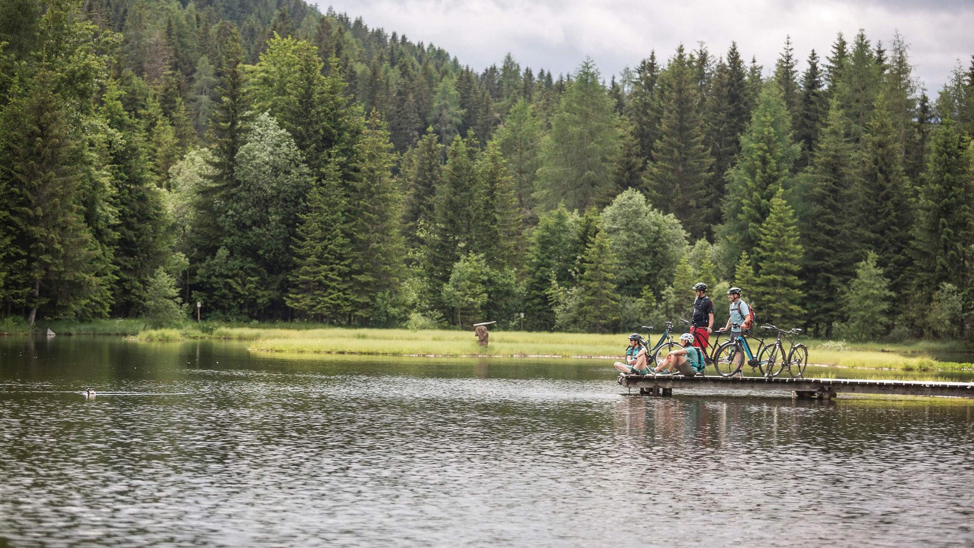 Cyclists on a pier by a lake in a forested area