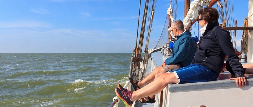 Two people relaxing on a sailboat with clear skies and sea
