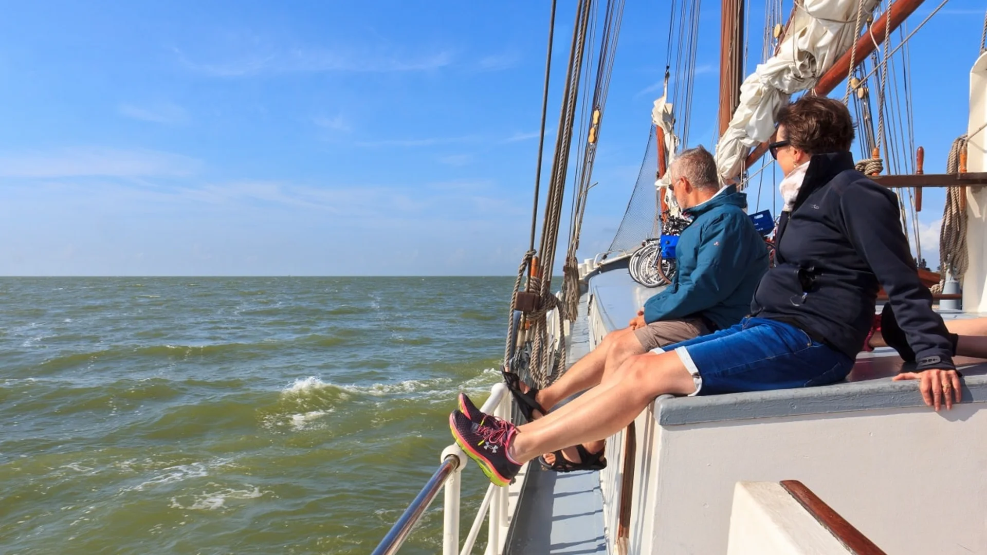Zwei Personen sitzen entspannt auf einem Segelboot bei klarem Himmel
