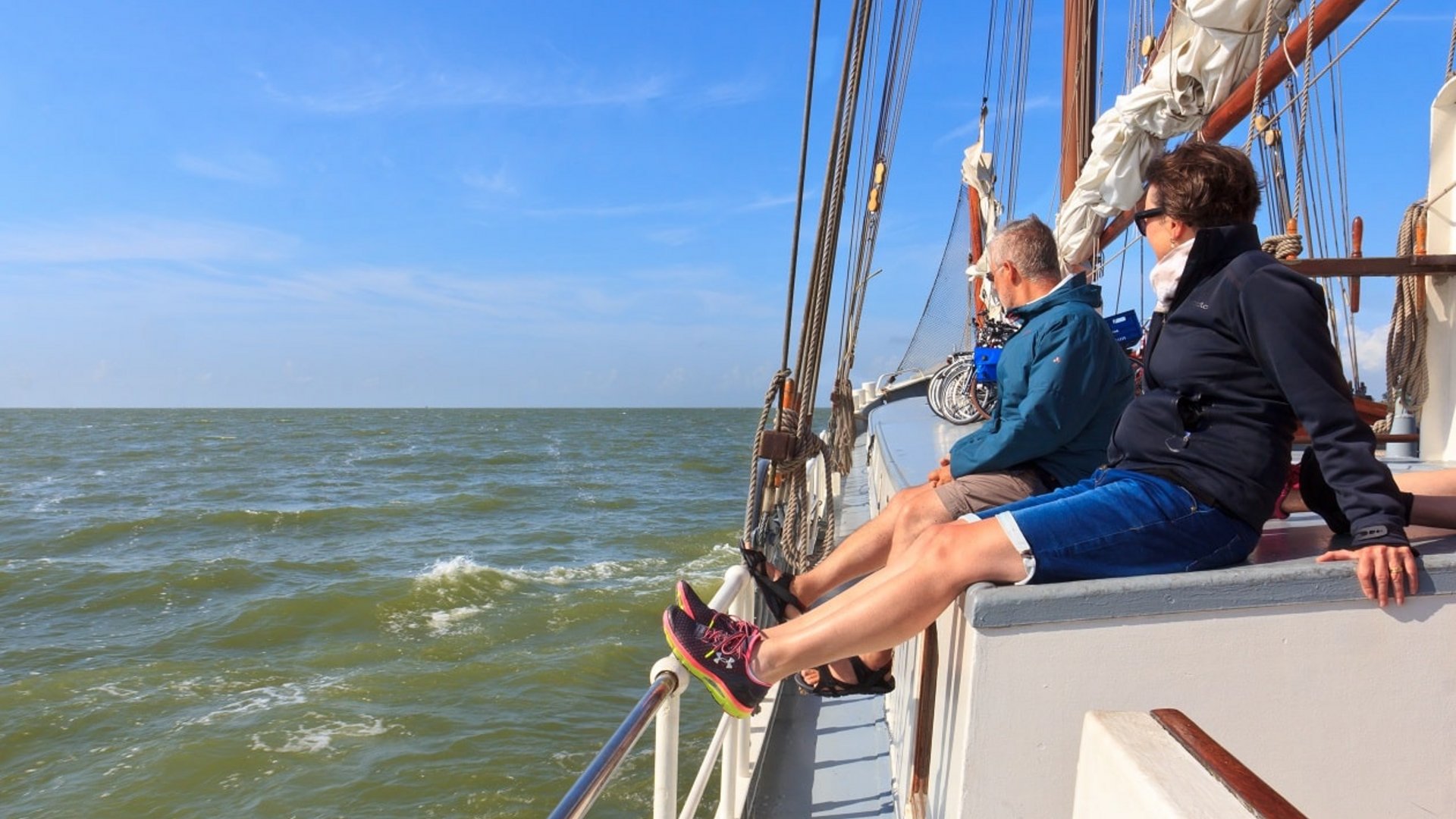 Two people relaxing on a sailboat with clear skies and sea
