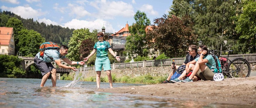 Friends relaxing and playing by the riverbank on a sunny day.