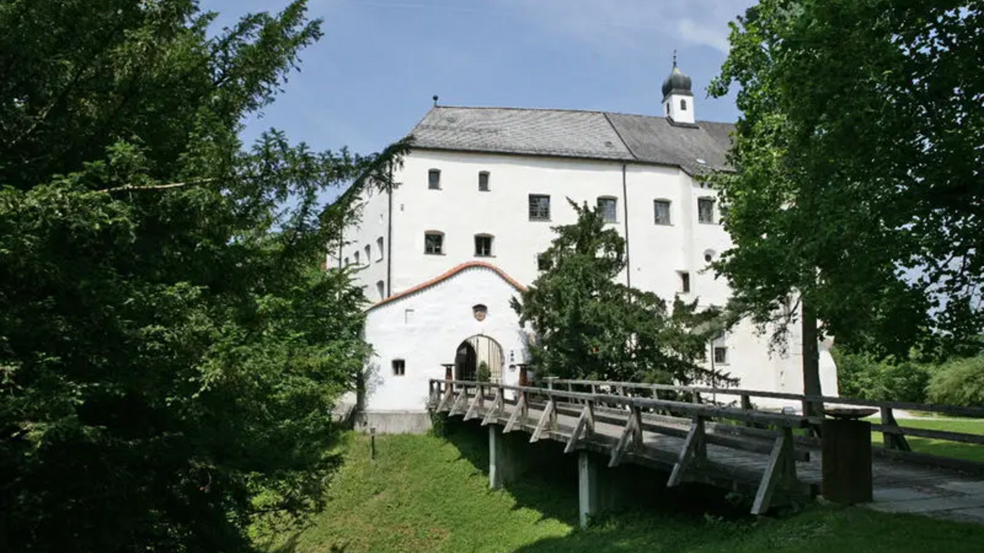 White castle with wooden bridge surrounded by green trees under clear sky