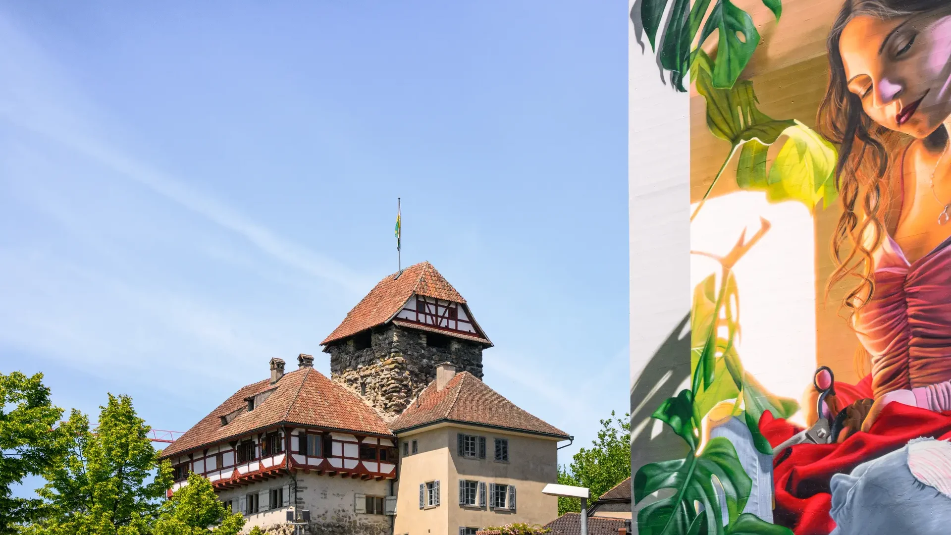 Tour-Detail © Balz Kubli Historisches Gebäude mit Turm neben großer bunter Wandmalerei einer Frau
