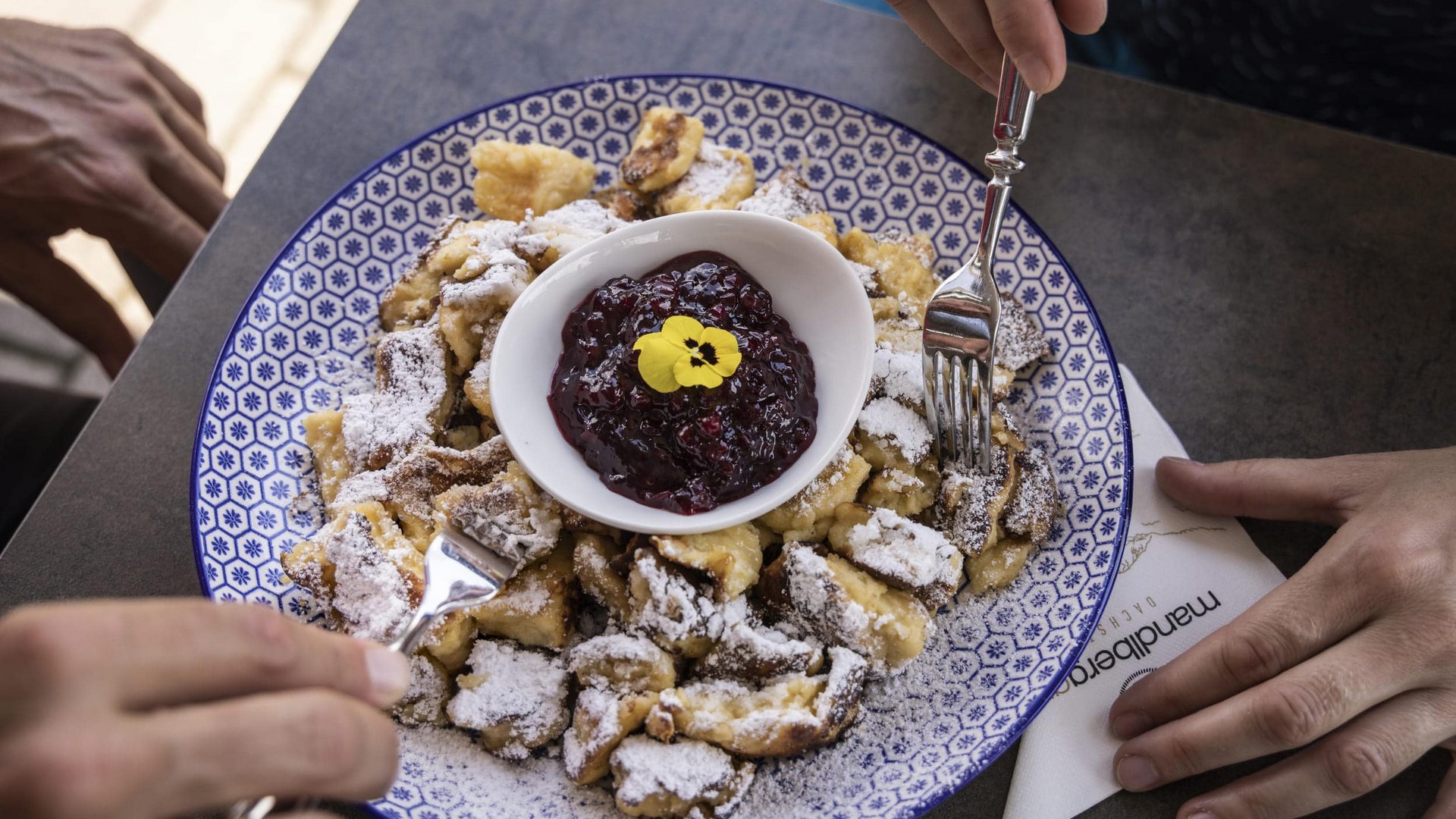 Kaiserschmarrn with powdered sugar and berry jam on a blue and white plate