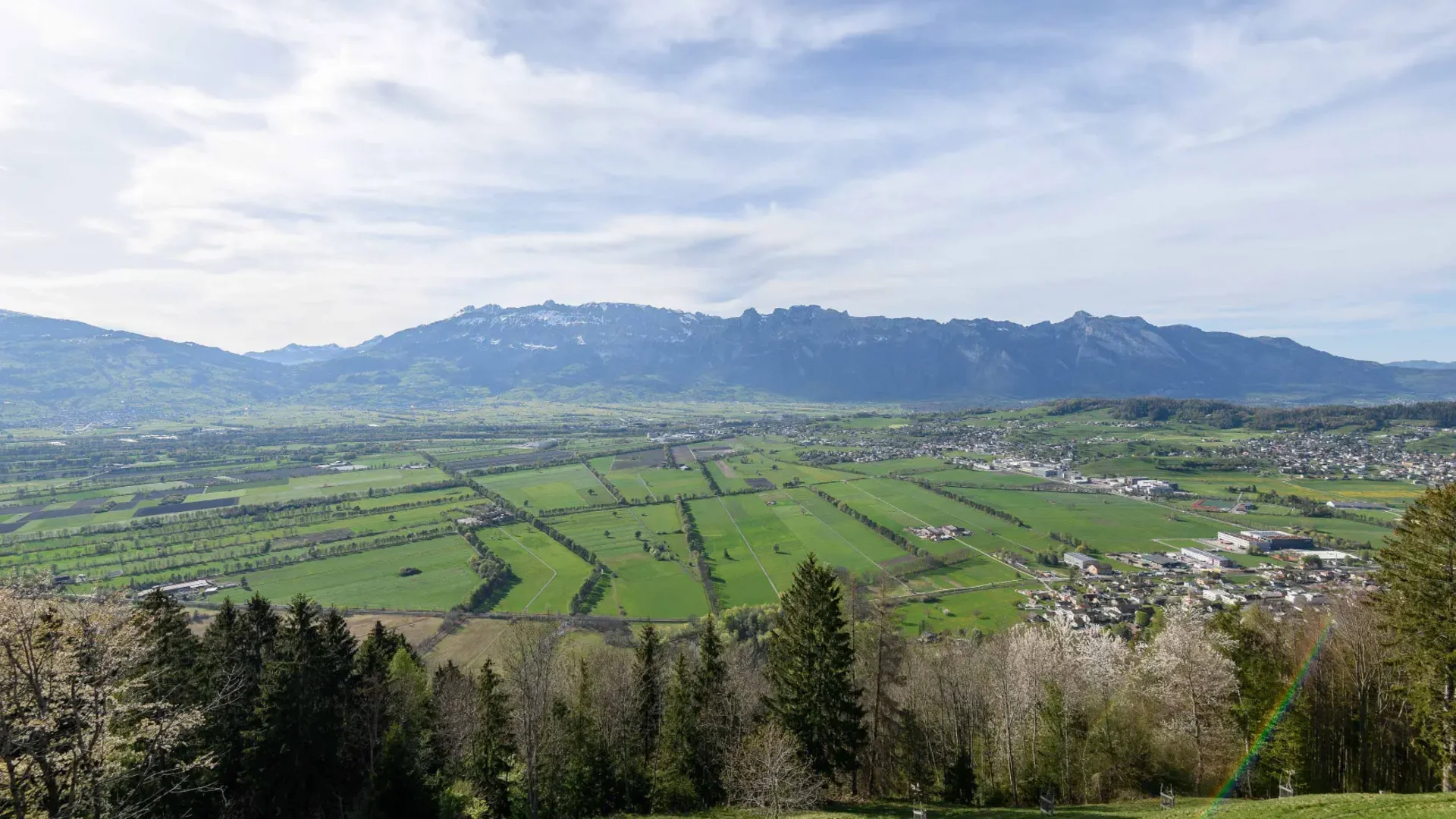 Blick auf grüne Felder und Berge unter bewölktem Himmel