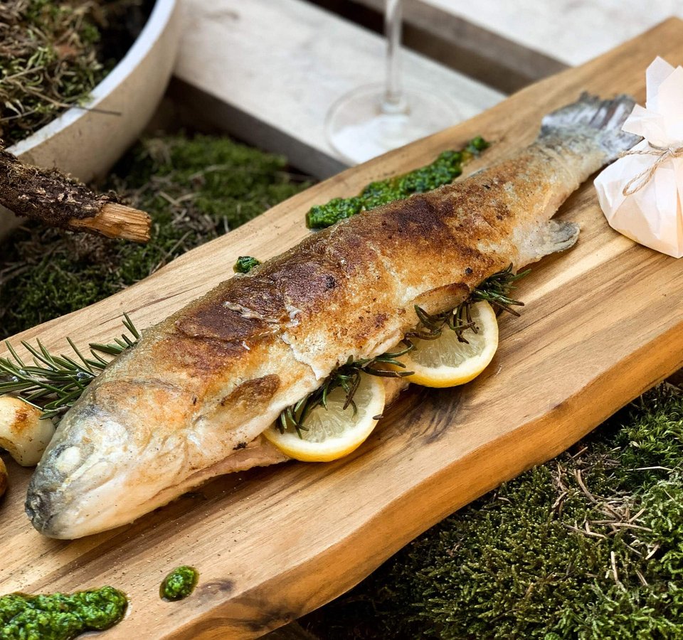 Grilled trout on wooden board with lemon slices and herbs
