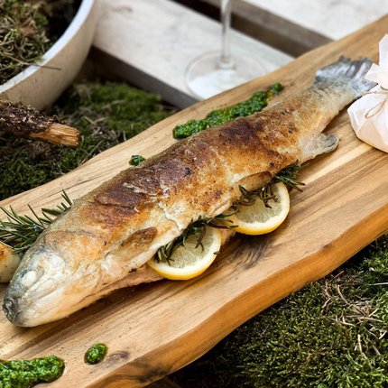 Grilled trout on wooden board with lemon slices and herbs