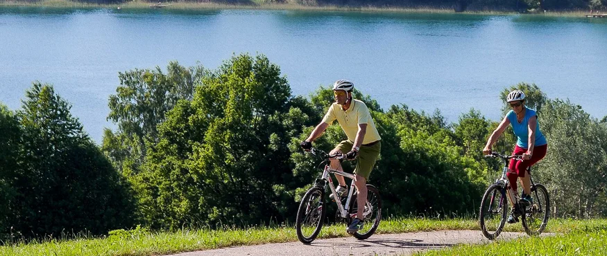 Two cyclists riding on a path beside a lake and trees