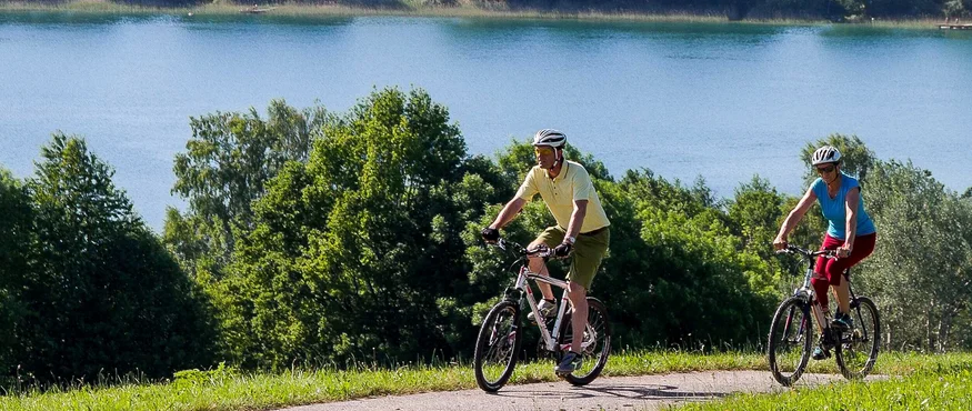 Zwei Radfahrer fahren auf einem Weg neben einem See und Bäumen