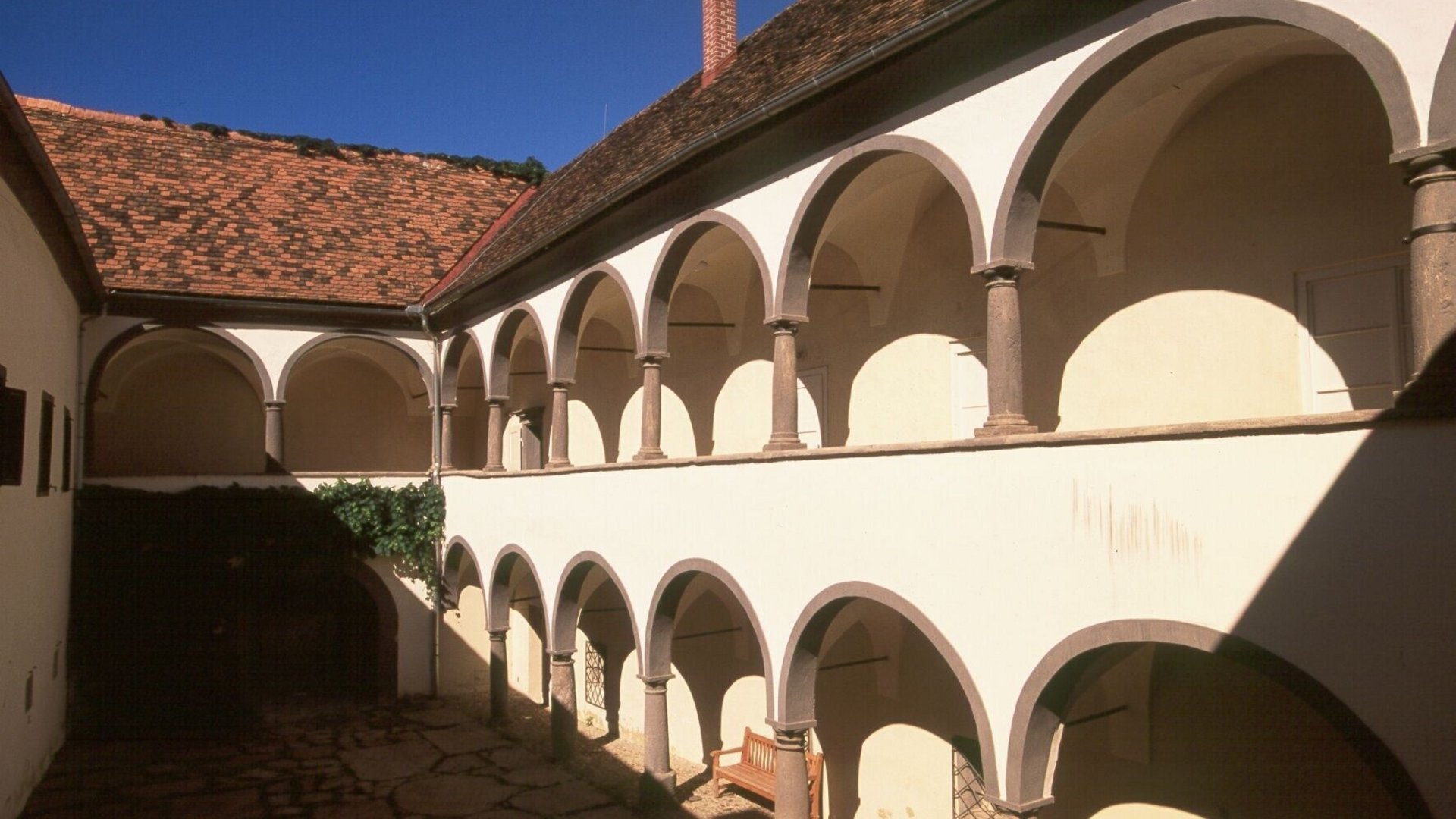 Courtyard with two-story arcade and tiled roof under clear blue sky