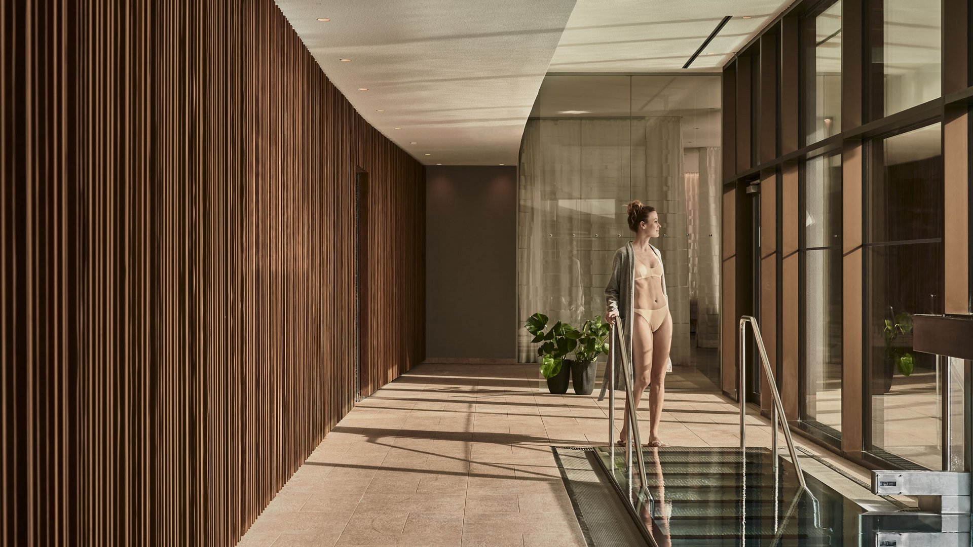 Woman in bathrobe standing by an indoor pool in a modern spa area