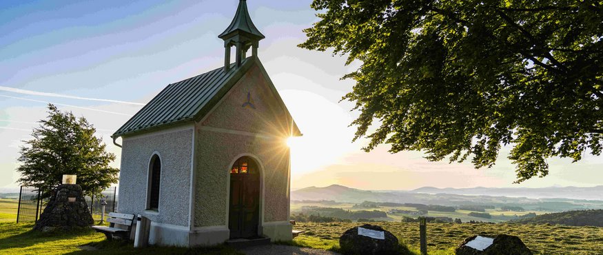 Kleine kapel bij zonsondergang met landschap en bomen op de achtergrond