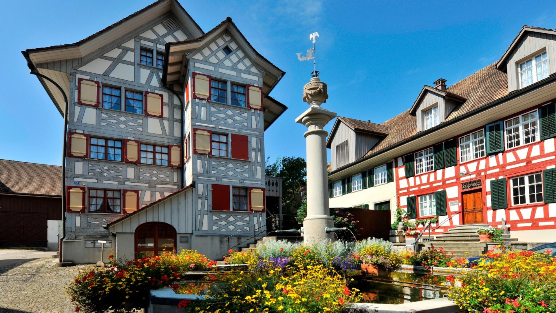 Historic half-timbered houses and flower-filled fountain in sunny village