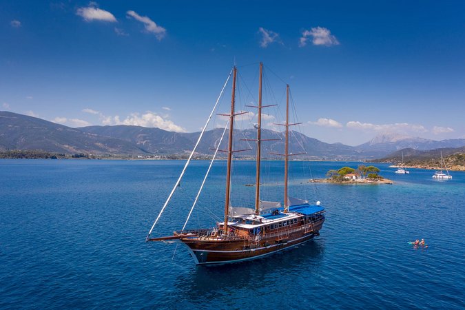 Segelschiff auf blauem Meer vor Insel und Bergen bei klarem Himmel
