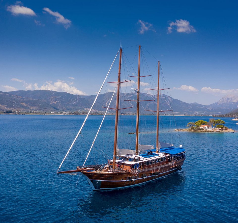 Segelschiff auf blauem Meer vor Insel und Bergen bei klarem Himmel