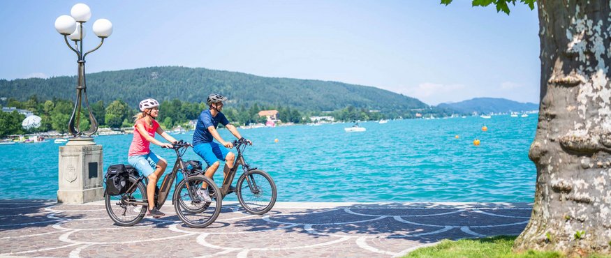 Two cyclists riding along a lakeside on a sunny day
