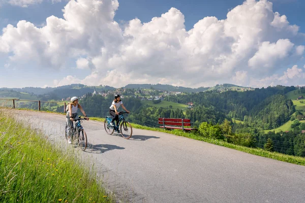Zwischen Klosterflair & Seensucht in St. Gallen © Thomas Staub Zwei Frauen fahren Fahrrad auf Bergstraße mit weitem Talblick und blauem Himmel