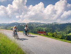 Two women cycling on mountain road with valley view and blue sky