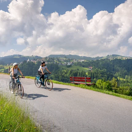 Twee vrouwen fietsen op bergweg met uitzicht op vallei en blauwe lucht