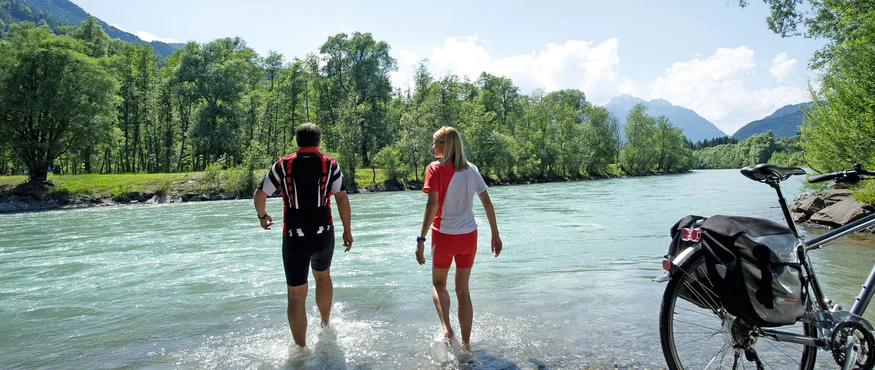Twee fietsers waden door de rivier naast hun fiets op een zonnige dag