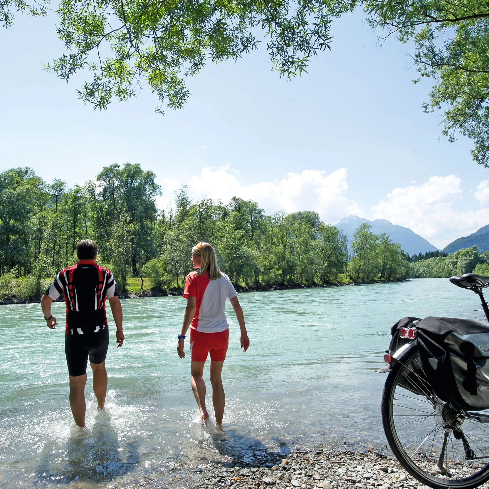 Zwei Radfahrer waten im Fluss neben ihrem Fahrrad an einem sonnigen Tag