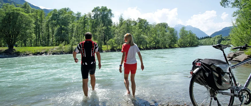 Zwei Radfahrer waten im Fluss neben ihrem Fahrrad an einem sonnigen Tag