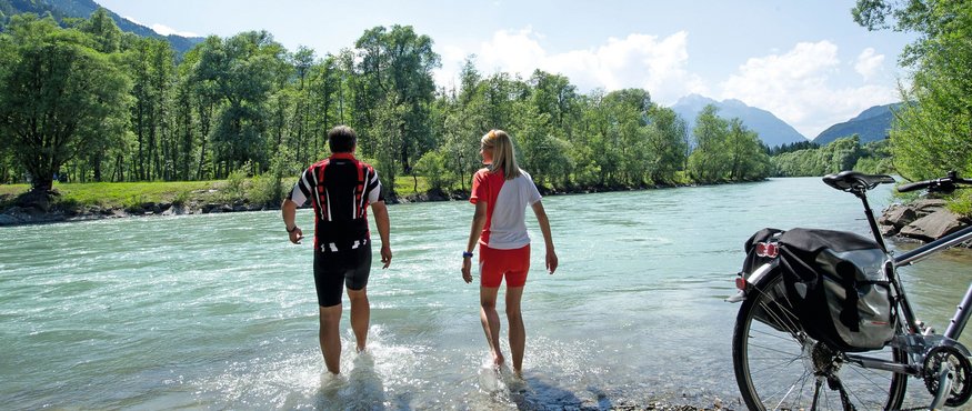 Two cyclists wading in the river beside their bike on a sunny day