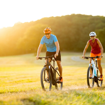 Two people riding mountain bikes on a field at sunset