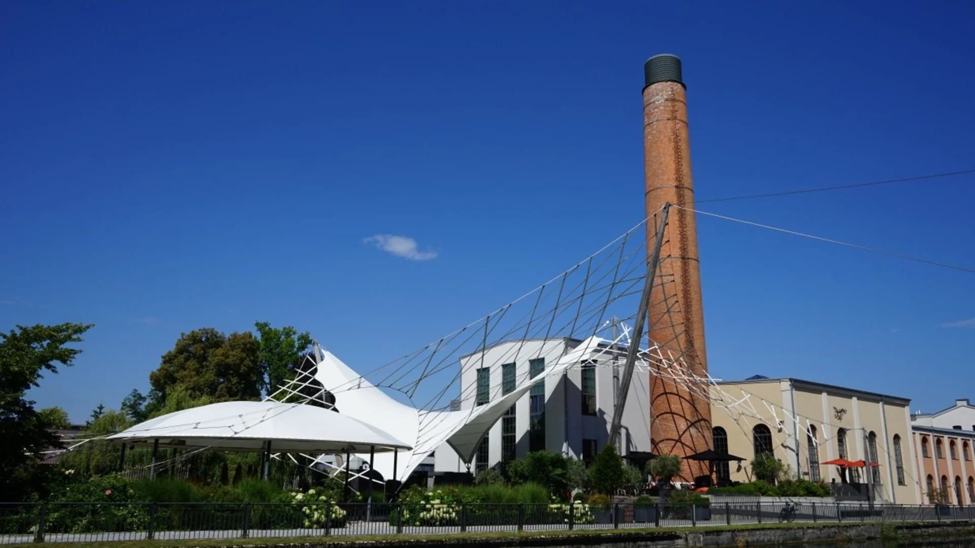 Altes Industriegebäude mit Schornstein und moderner Zeltdachkonstruktion am Wasser
