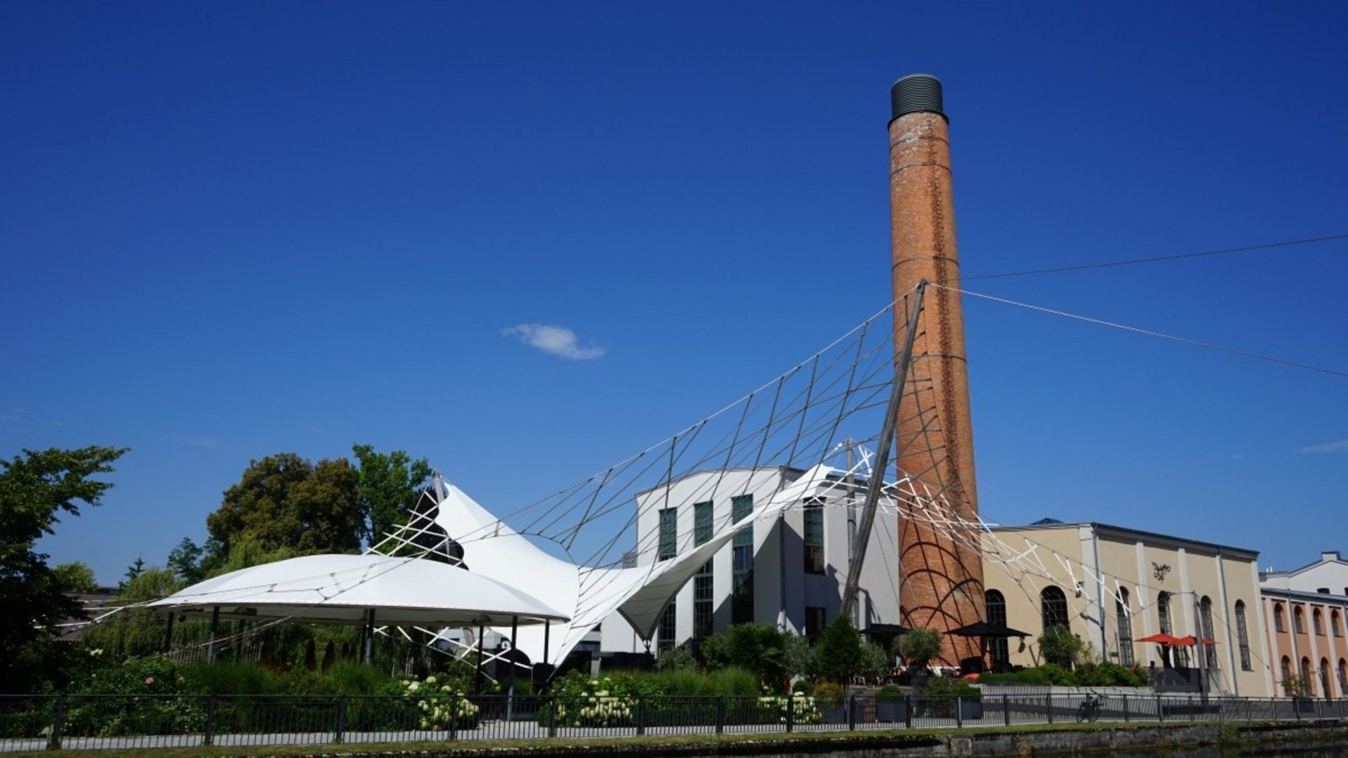 Old industrial building with chimney and modern tent roof structure by water
