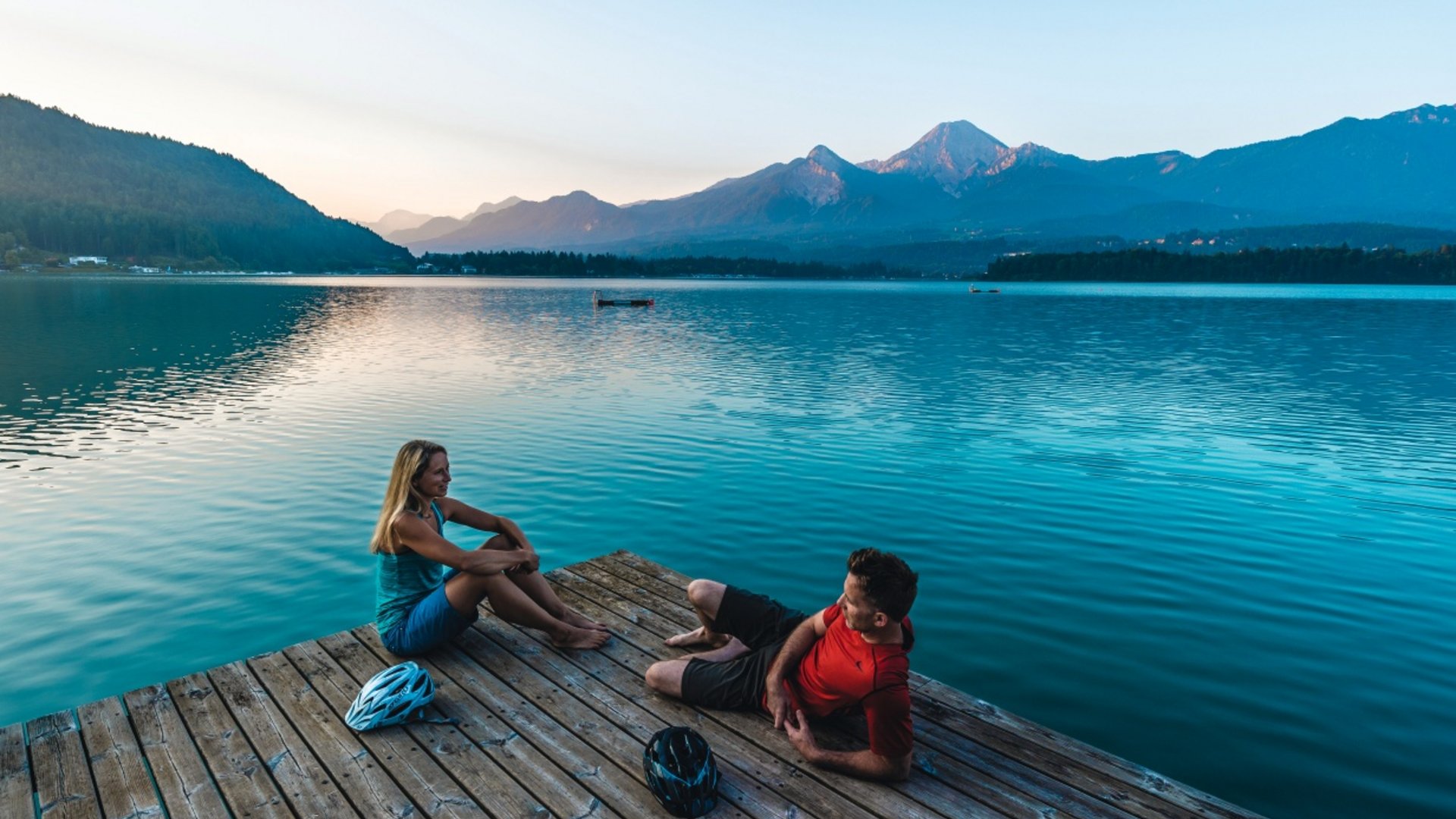 Couple relaxing on a dock by the lake with mountains in the background at sunset