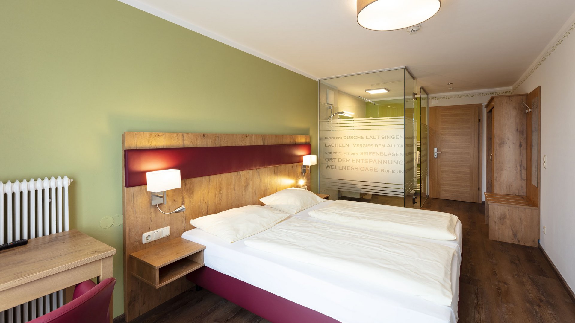 Modern hotel room with double bed, desk, and glass shower