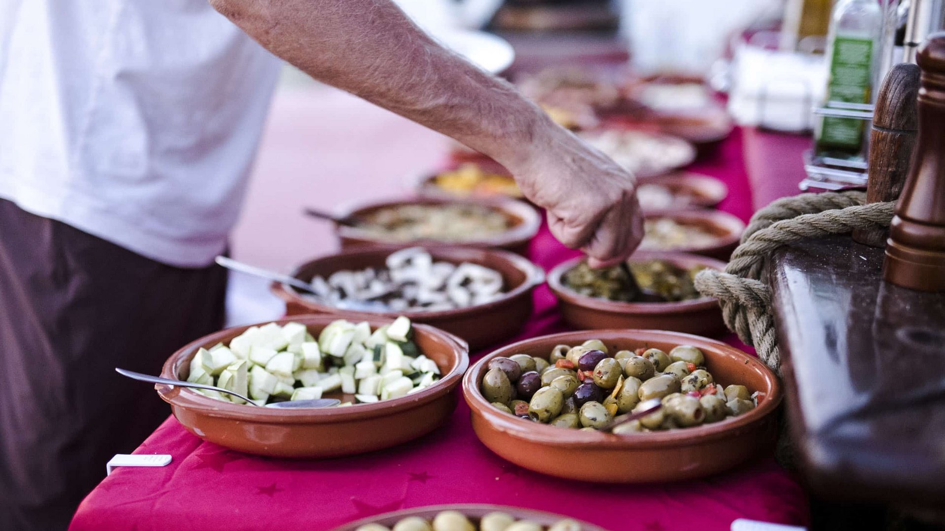 Hand picking olives from a bowl on a buffet with various snacks