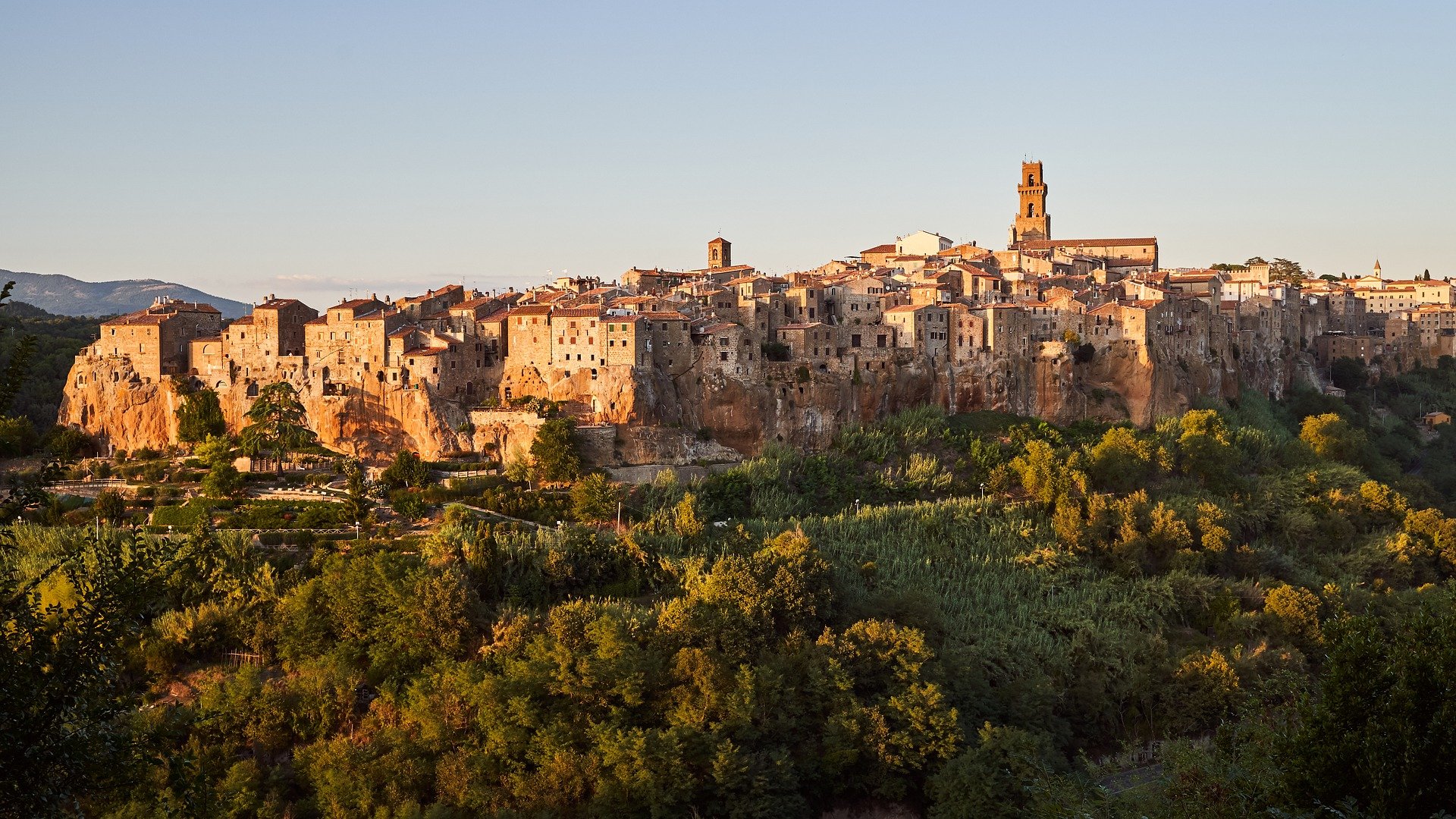 Historic town built on a cliff with green trees surrounding it at sunset