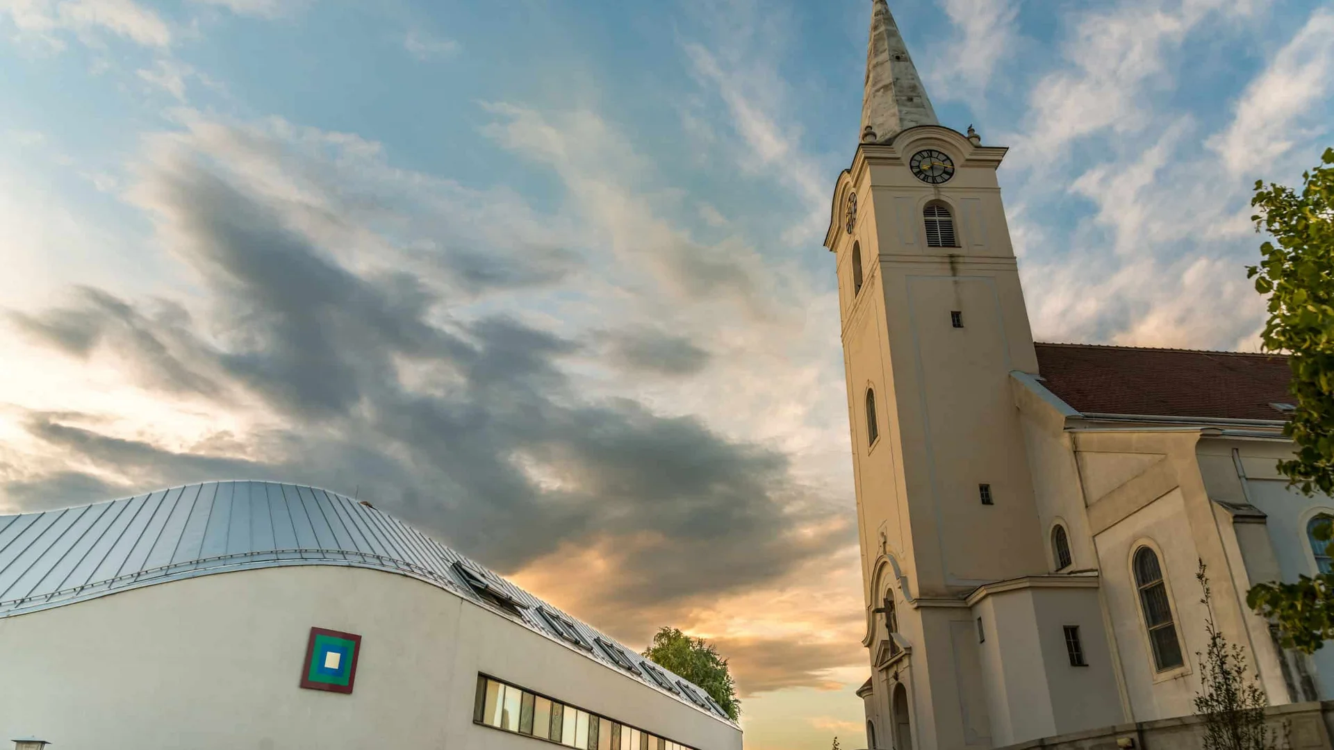 Kerk toren naast modern gebouw bij zonsondergang met bewolkte lucht