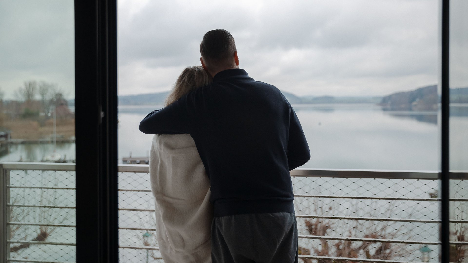 Couple hugging on balcony overlooking lake under cloudy sky