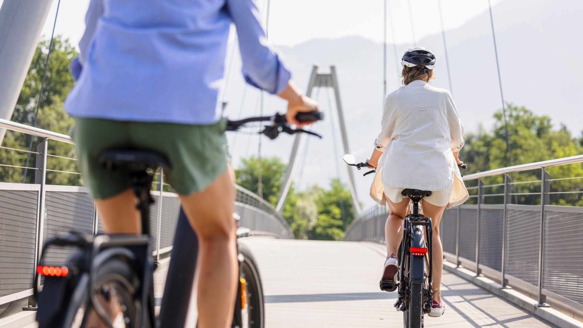 Two people riding bicycles on a bridge on a sunny day.